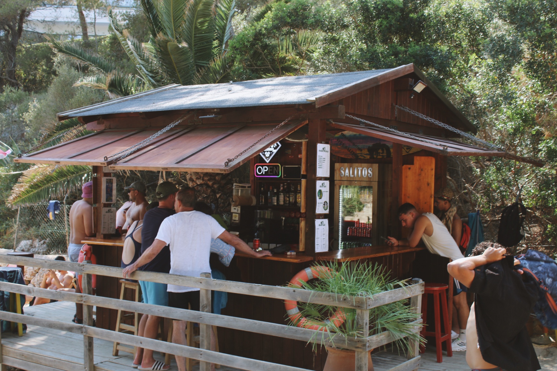 A small wooden beach bar tucked into the pines above the cove, guests ordering drinks
